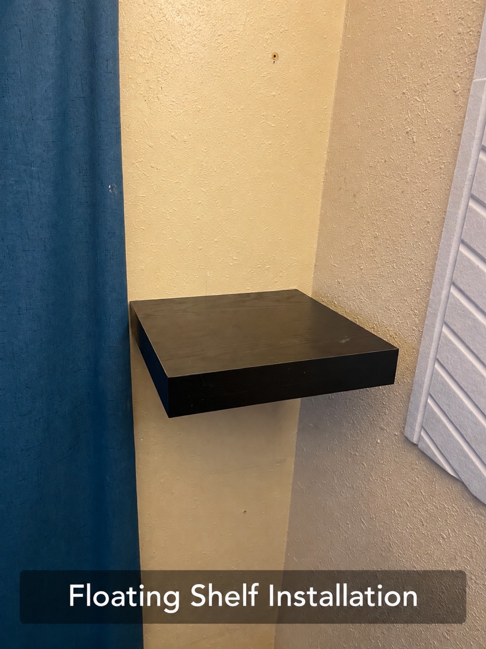 Dark floating shelf installed on a wall beside a window